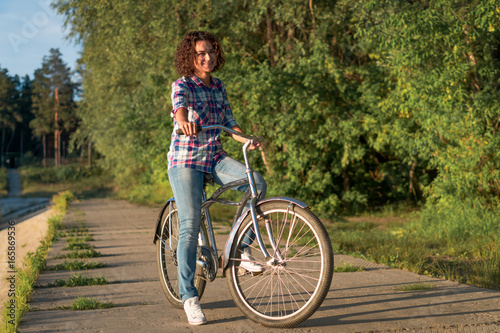 Young woman on a bicycle in the park on a sunset background 
