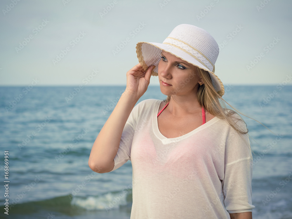 Beautiful woman in hat against the evening sea.