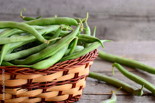 Fresh green string beans in a wicker basket. Young green beans, good source of fiber, vitamins and minerals. Wooden background