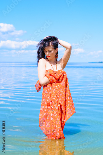 A beautiful stylish young woman with thin figure in cloth rest and relaxes on the beach in the morning, in blue water 
