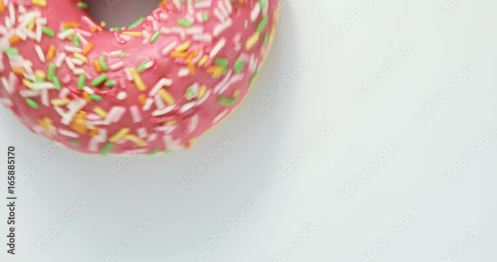 Bright and colorful sprinkled donut close-up macro shot spinning on a white background. Delicious sweet donut rotating on a plate. Top view Bright and colorful sprinkled donut close-up macro shot spinning on a white background. Delicious sweet donut rotating on a plate. Top view