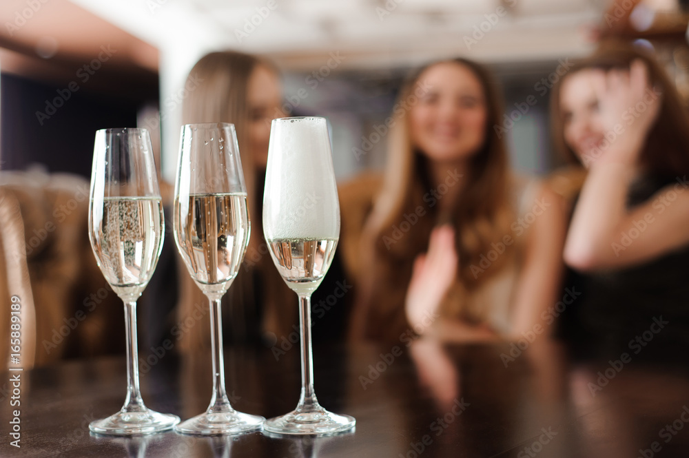 Man fills glasses of champagne for three beautiful young women in restaurant Man fills glasses of champagne for three beautiful young women in restaurant