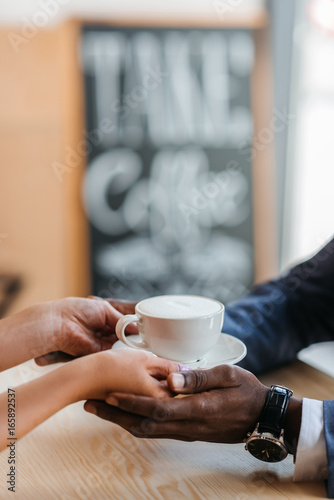 cropped view of waitress giving cup of coffee to african american businessman in cafe