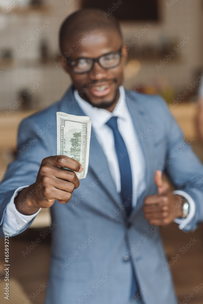 selective focus of african american businessman holding money and showing thumb up