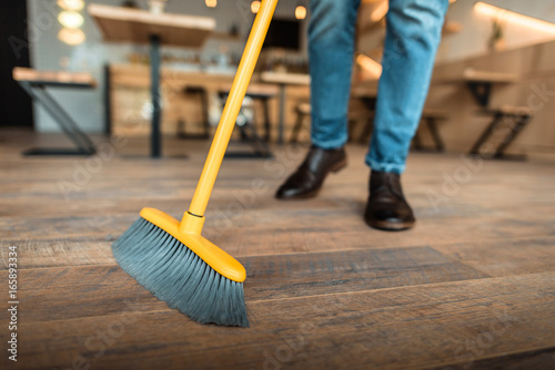 cropped view of african american worker sweeping with broom in coffee shop photo