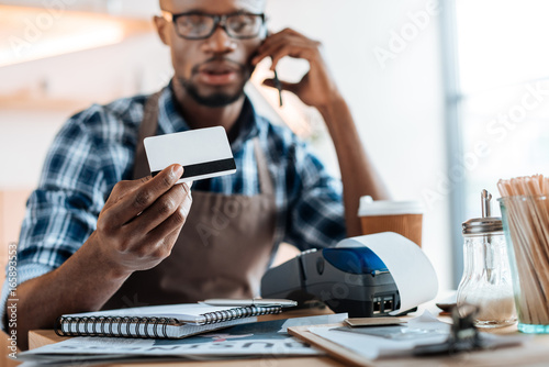 african american male owner working with credit card reader and smartphone in coffee shop photo