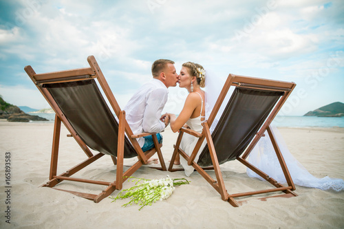 Bride and groom kissing in lounge chair by the sea on their wedding day