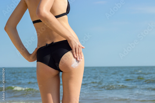 Suntan Lotion Woman Applying Sunscreen Solar Cream. Beautiful cute girl applying Sun Tan Cream on her skin on the beach. Sun Tanning. Skin care and Protection. Vacation