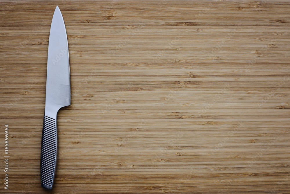 Stainless kitchen knife on empty cutting board.