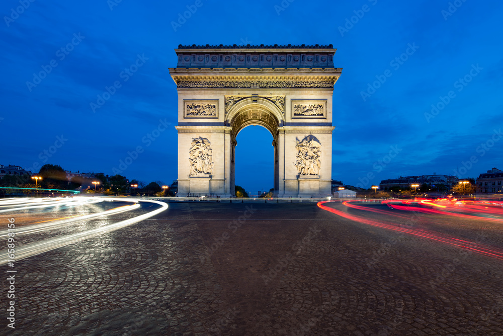Paris street at night with the Arc de Triomphe in Paris, France.