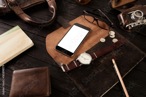 Mockup - Black phone with leather bag, old watch, glasses and book on dark wooden board