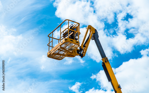 Hydraulic lift platform with bucket of yellow construction vehicle, heavy industry, blue sky and white clouds on background photo