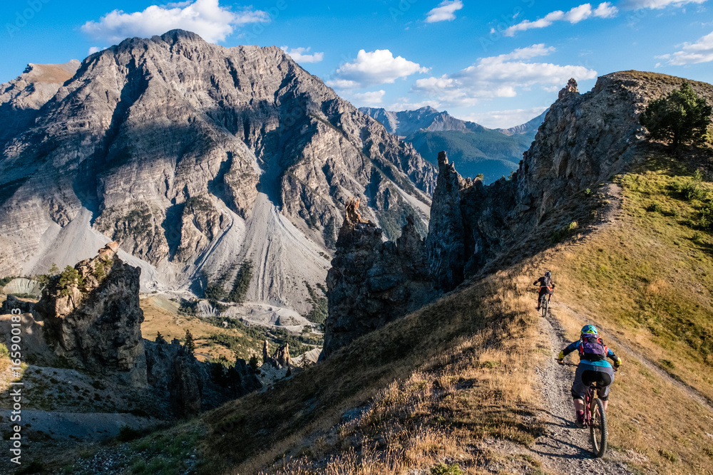 Alpine Mountain bikers ride along a ridge with epic views behind