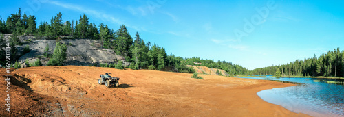 Quad ATV stands on sandy terrain at a beautiful lake.
