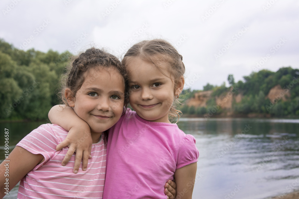 In the summer, two young friends stand embracing on the river bank. In the summer, two young friends stand embracing on the river bank.