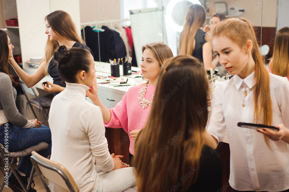 Three professional make-up artists work with beautiful young women. School of professional make-up