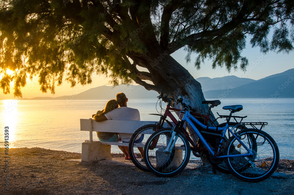 Fototapeta premium A couple of lovers watching the sunset sitting on a bench by the sea.