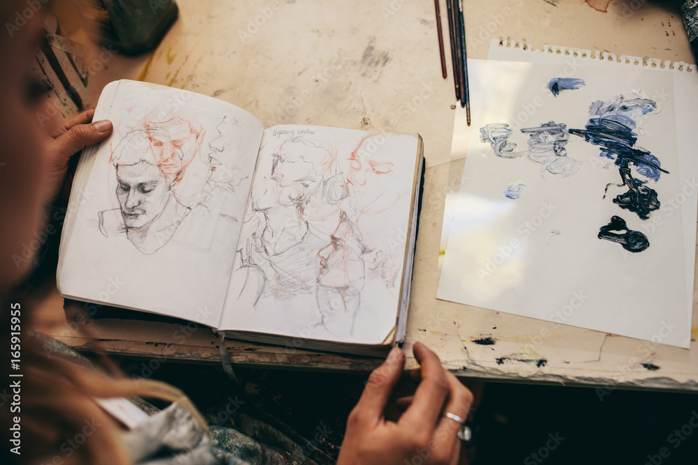 Female artist looking at sketches in her studio - obrazy, fototapety, plakaty 