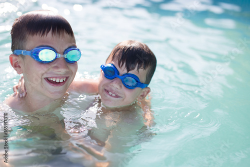 Happy little kids in goggles playing in swimming pool