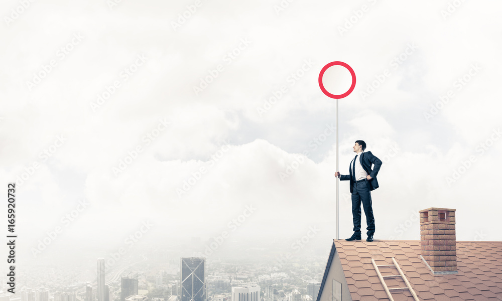 Caucasian businessman on brick house roof showing stop road sign Caucasian businessman on brick house roof showing stop road sign
