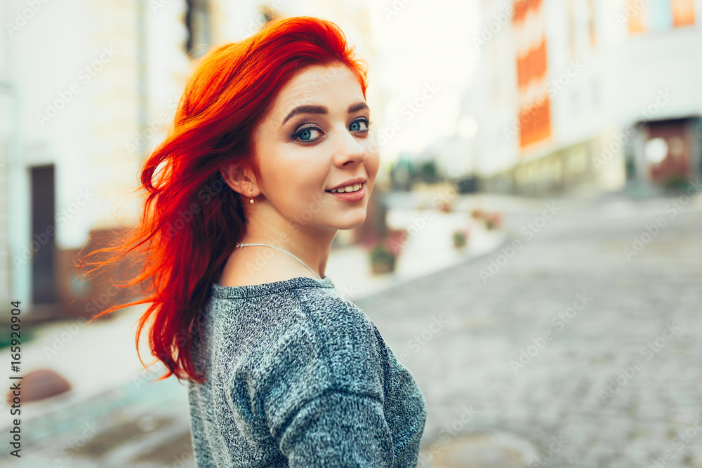 Startled young redhead woman looking back over her shoulder at the camera as she strolls down a deserted urban street