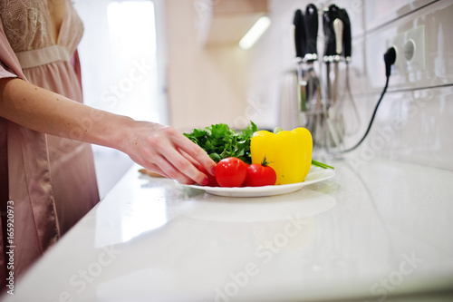Portrait of an attractive young woman in robe making salad out of fresh vegetables in the kitchen.