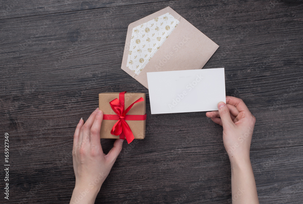 Female hands holding gift card and gift box over the black wooden table