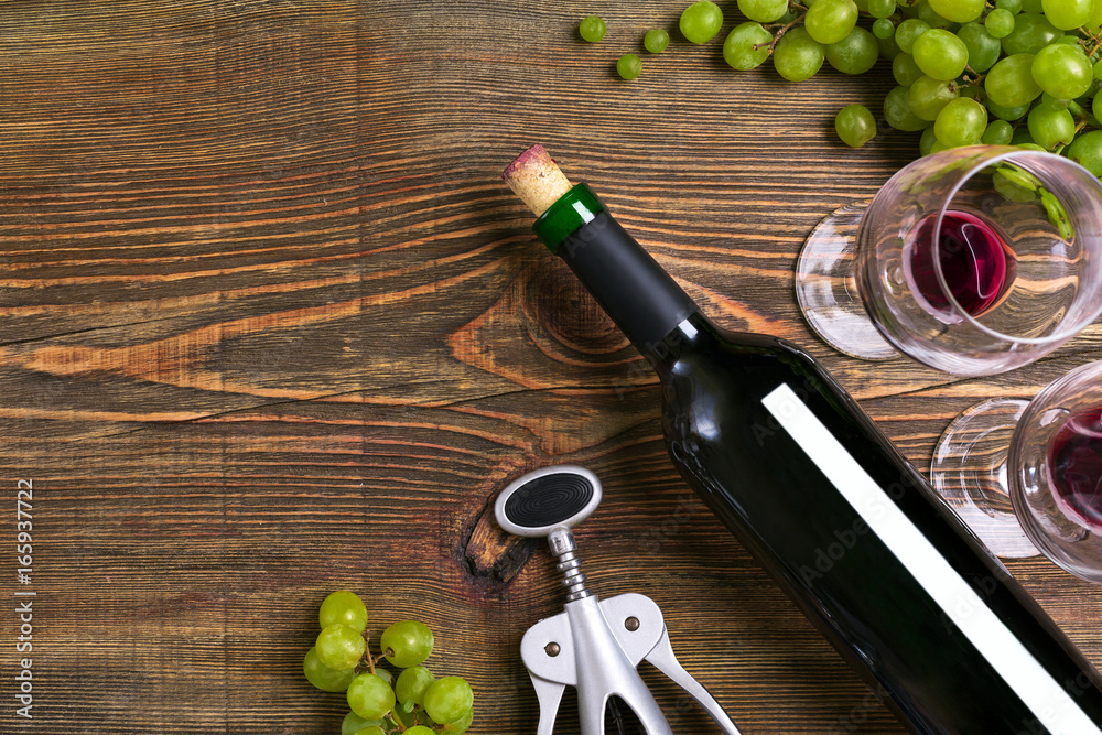 Obraz premium Red wine bottle, grape, chocolate and glasses over wooden table. Top view with copy space