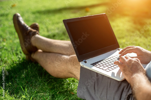 Cropped shot of man using laptop with blank screen while sitting on green grass photo