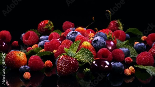 Fresh juicy berries: strawberry, cherry, blueberry, raspberry, gooseberry and mint leaves rotate on black mirror background in 4K. Vivid closeup shot of mixed tasty fruits.
