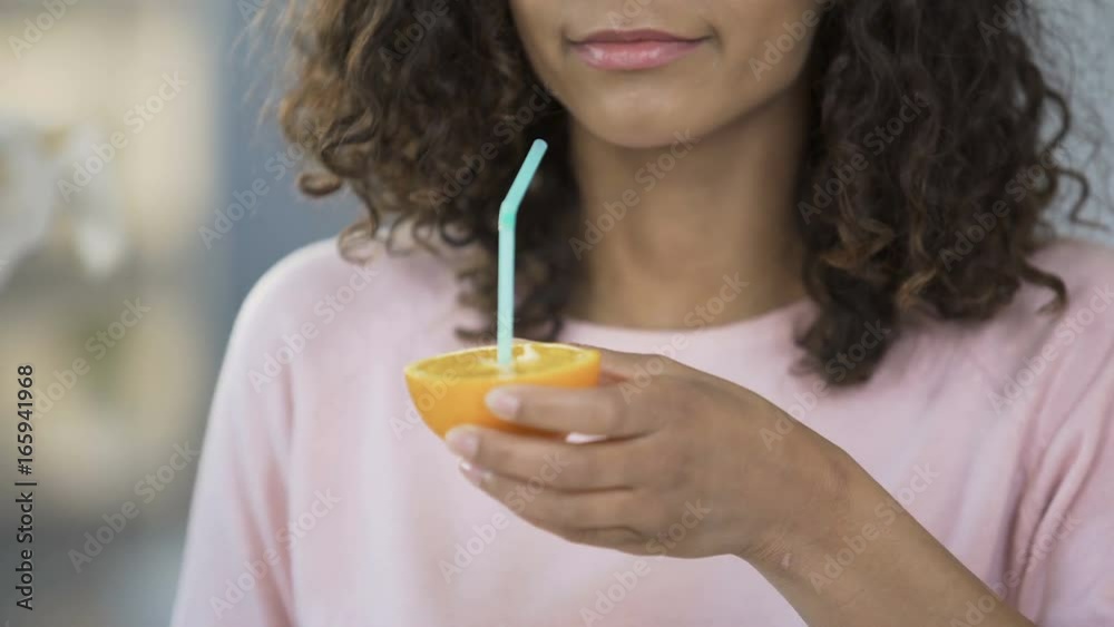 Multiracial woman drinking juice from orange half, health care, nutrition Multiracial woman drinking juice from orange half, health care, nutrition