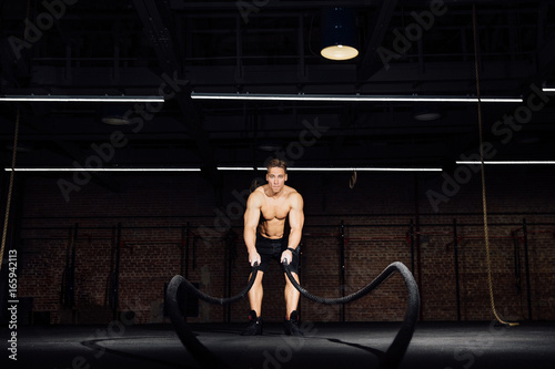 Fitness man workout with battle ropes at gym. training exercise fitted body in club. Torso. photo