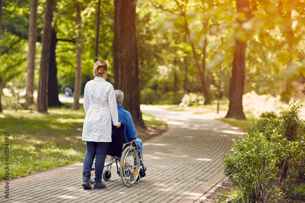 Fototapeta premium nurse helping elderly man on wheelchair outdoor.
