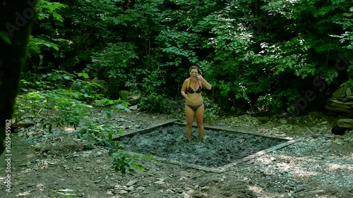 Woman tourist in a bathing suit is smeared with curative clay on the nature of a mountain forest. girl skin treatment