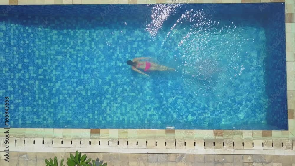 AERIAL TOP DOWN: Young woman on summer vacation jumping head first into blue pool water for refreshment on hot sunny day. Girl in pink bikini diving into clear pool water in empty luxury resort