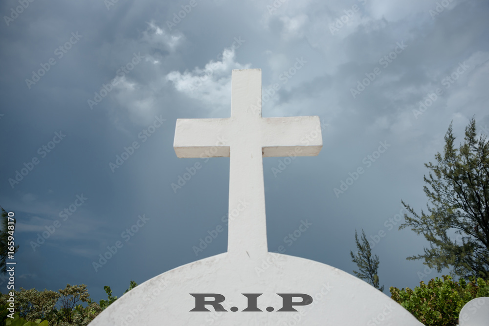 White cross above letters RIP on headstone under foreboding dark cloudy sky. White cross above letters RIP on headstone under foreboding dark cloudy sky.