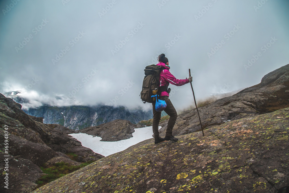 Fototapeta premium Girl stands on the peak of sandstone rock . Beautiful moment the miracle of nature. Morning mountain background. Girl watch foggy miracle. Trolltunga hiking route