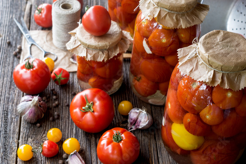 Tomato preserves in the jars  raw tomato fruits and seasonings on the wooden gray background