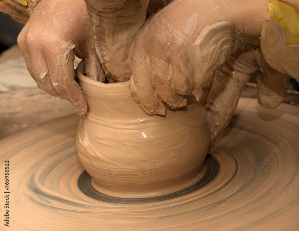 Beginner and teacher in process of making clay bowl on pottery wheel
