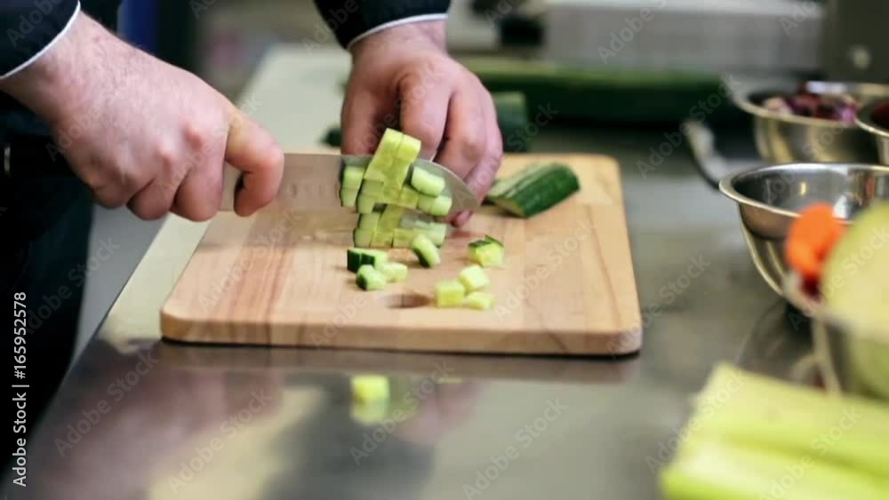 hands of male cook chopping cucumber in kitchen