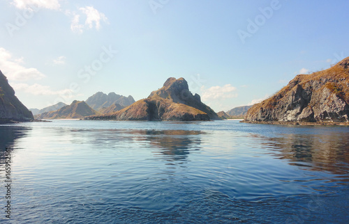 Coastline of mountains with green vegetation reflected in blue ocean water at Labuan Bajo in Flores, Indonesia.