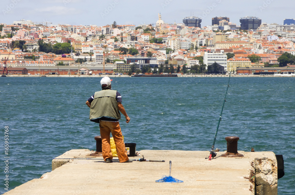 A man fishing in river Tagus - Lisbon's cityscape in the background