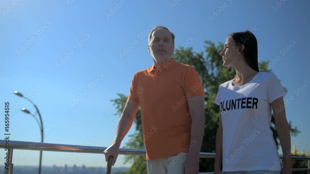 Pleasant aged man walking with a positive female volunteer Pleasant aged man walking with a positive female volunteer