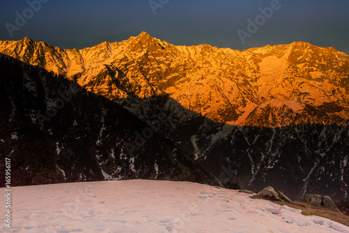 White snow mountains turned golden due to suns rays at golden hour or sunset at Triund, Mcleod ganj, Dharamsala, himachal pradesh, India. Mind blowing scene. golden mountains, hills, camping, dusk photo