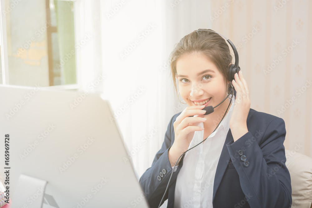 Young beautiful girl working at a laptop in a small medium enterprise. She is operating the phones and computer Young beautiful girl working at a laptop in a small medium enterprise. She is operating the phones and computer