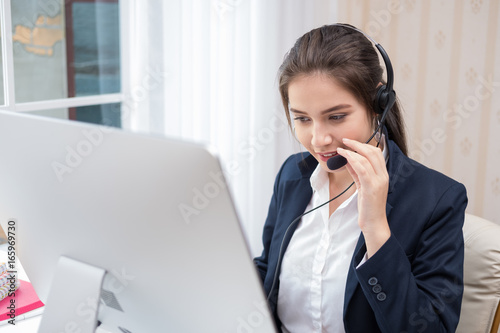 Young beautiful girl working at a laptop in a small medium enterprise. She is operating the phones and computer