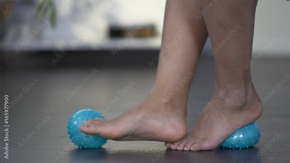 Female rolling feet on massaging ball, stretching bottom of foot, pain