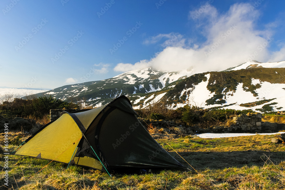tent camp high in the mountains in front of snow and fog covered peak during spring ascent adventure travel