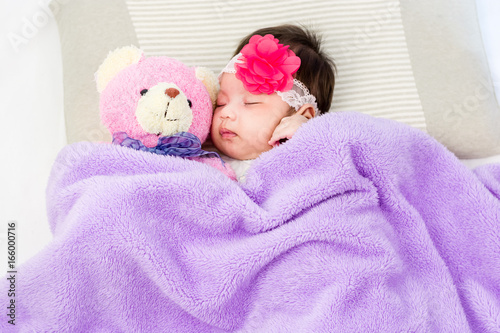 Portrait of sleeping baby  lying on a bed with head band and bear doll