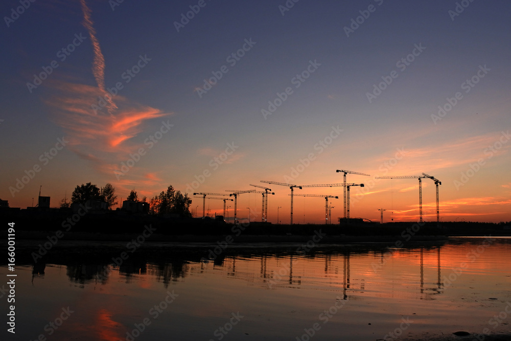 Construction cranes on a background of a stunning sunset